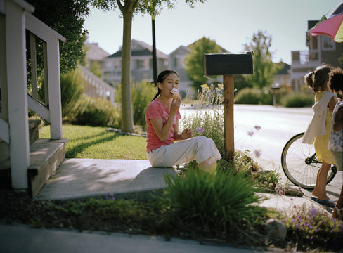 Portrait of teenage girl sitting by her letterbox eating an ice cream.