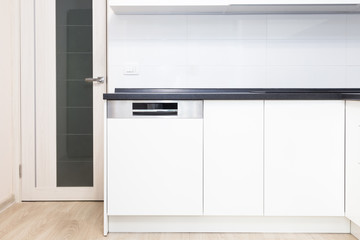 Build-in dishwasher in a white kitchen with black counter top. 