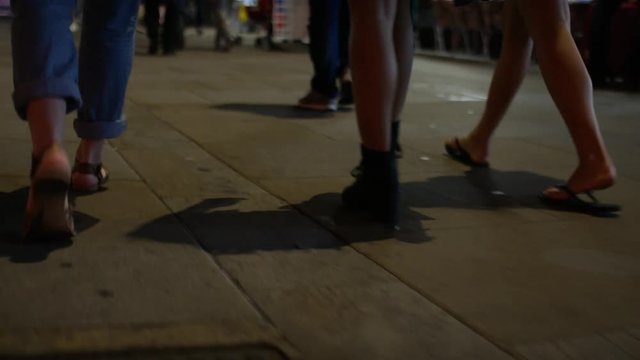 Legs of three females walking along a sidewalk in the city at night