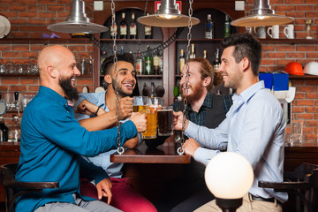 Man Group In Bar Clink Glasses Toasting, Drinking Beer Hold Mugs, Mix Race Cheerful Friends Wear Shirts