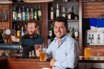 Young Man In Bar Hold Glasses Sit At Counter, Drinking Beer