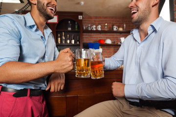 Two Man In Bar Clink Glasses Toasting Sit At Table, Drinking Beer Hold Mugs Close Up