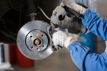 Brand new brake disc on car in a garage. Auto mechanic repairing  .