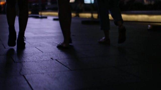 Silhouette legs of three female legs walking through the city at night