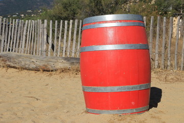 Bright red wooden barrel on a beach in tropical beach paradise with trees and rustic fence