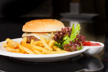 Cheeseburger with French fries, lettuce and ketchup lying on a s
