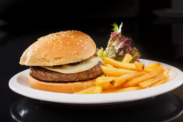 Cheeseburger with French fries, lettuce and ketchup lying on a s