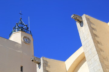 Gargoyles, bell tower and clock tower against blue sky on a church in the South of France