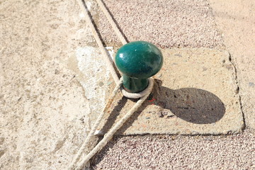 Green bollard on stone quayside with ropes mooring sailing boats