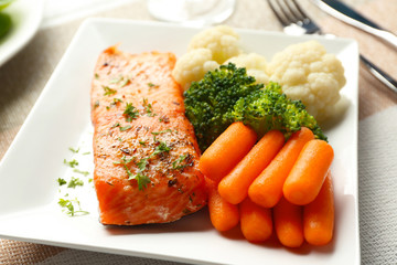 Piece of salmon with vegetables on plate closeup