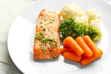 Piece of salmon with vegetables on plate closeup