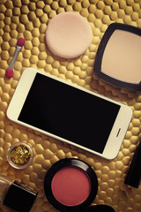Decorative cosmetics and smartphone on golden background