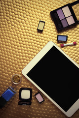 Decorative cosmetics and tablet on golden background
