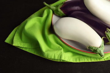 Fresh eggplants on plate with green napkin on black background