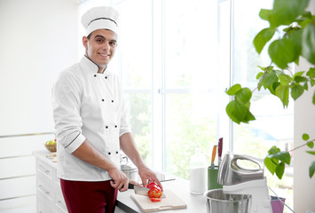 Young chef cook cutting fresh pepper in kitchen