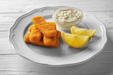 Plate with tasty fish nuggets, lemon slices and sauce on wooden table