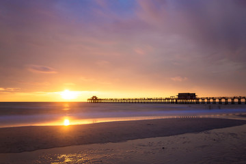 The sun goes down at the Naples Pier in the Gulf of Mexico, Southwest Florida, USA. Amazing landscape spot of the sun coming down at blue hour in this idyllic place for family vacation and relax.