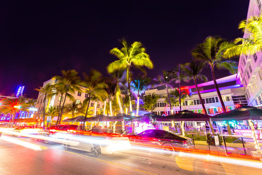 Ocean Drive scene at night with neon lights, palm trees, cars and people having fun, Miami beach.