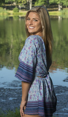 Beautiful young Caucasian woman in blue print romper poses near lake in a park - fashion model