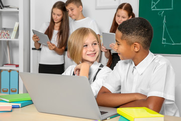 Fototapeta premium Schoolchildren sitting in classroom with laptop