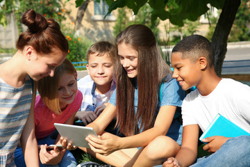 Schoolchildren with mobile phone and tablet computer sitting on grass