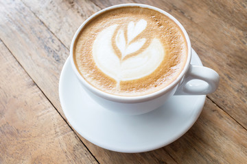 Cup of coffee with heart pattern in a white cup on wooden backgr