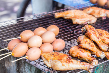 Local bbq with egg skewers and chicken legs on a grill at a market in thailand