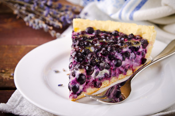 Bilberry, blueberry tart with lavender on white plate, wooden background