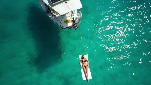 aerial view of a woman relaxing on raft next to sailboat in the Caribbean