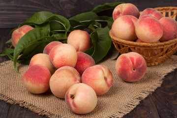 peaches in a wicker basket with leaves on wooden table