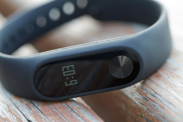 Black fitness watch with time on the display. Fitness tracker on the wooden surface. Closeup.