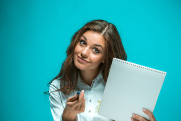 Fototapeta na wymiar Surprised young business woman with pen and tablet for notes on blue background