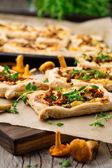 Homemade tarts of puff pastry with seasonal chanterelle mushrooms, cheese, thyme and onion on rustic wooden table, selective focus