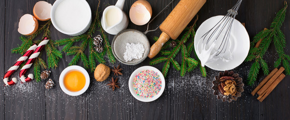 Baking ingredients for homemade Christmas pastry on dark rustic wooden background. Bake sweet cake dessert concept. Top view, long web format - obrazy, fototapety, plakaty