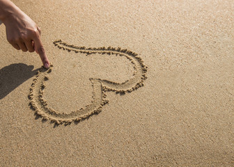 Fototapeta na wymiar Woman's hand drawing a heart in the sand.