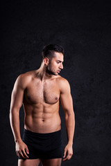 Fototapeta na wymiar Sexy and expressive shirtless male model flirting against black background 