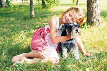 Naklejka na ściany i meble Cute little girl sitting on the grass in the garden with the dog