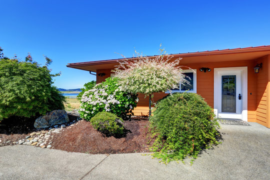 American Orange House Exterior. Flower Bed And Bushes In Front