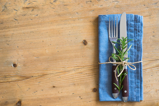 Fork, knife and napkin decorated with rosemary and thyme on wooden rustic background