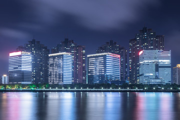 River And Modern Buildings Against Sky at night.