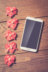 Red hearts and white smart phone with blank screen on an old wooden table