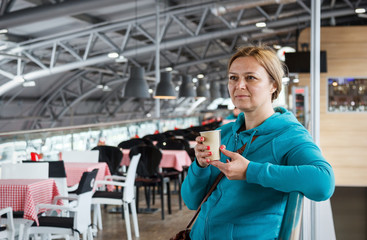 Caucasian woman standing with coffee at international airport while waiting for her flight. Female passenger at terminal.