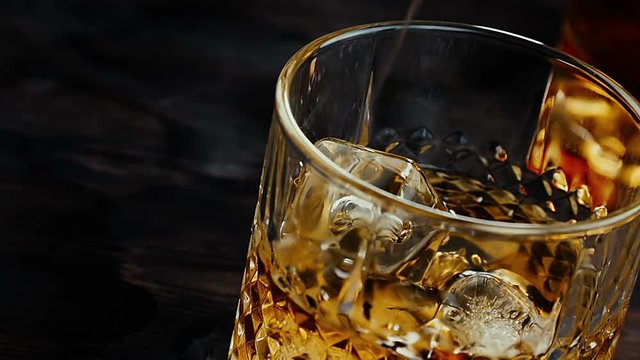 close-up of barman pouring whiskey in the glass with ice cubes on wood table, time of relax with whisky