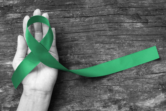 Emerald Green/ Kelly green color ribbon on human hand, clipping path: Satin fabric symbolic logo raising support help people life living with liver, gallbladder bile duct cancer illness