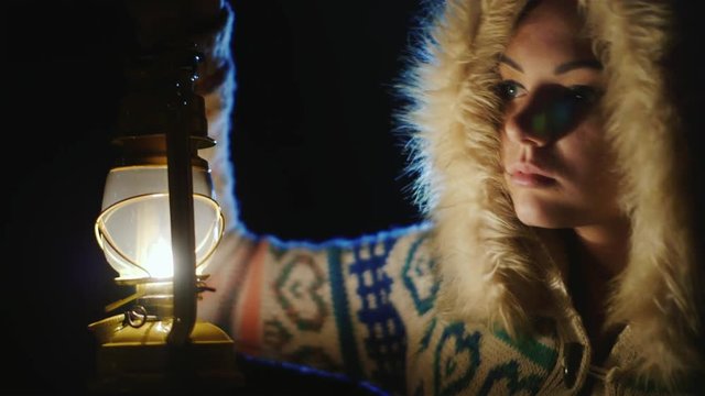 Young woman with an oil lamp in the dark. Fearfully looking around