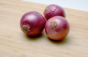 Three red onions on wooden background