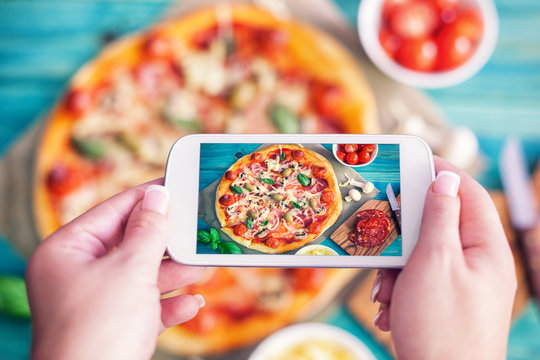 Young woman taking a photo of Pizza and Ingredients with smartphone 