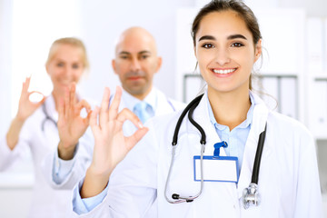 Fototapeta premium Happy doctor woman with medical staff at the hospital. Thumbs up and Ok sign!