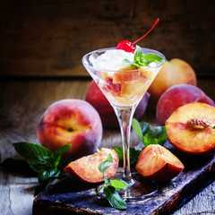 Dessert of peaches and yoghurt in martini glass, dark wood backg