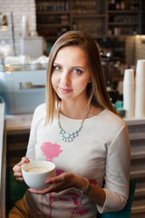 Happy beautiful young woman drinking coffee in cafe